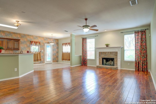 unfurnished living room featuring dark wood-type flooring, ceiling fan, a fireplace, and a wealth of natural light