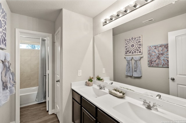 bathroom featuring hardwood / wood-style floors, vanity, shower / bath combo with shower curtain, and a textured ceiling