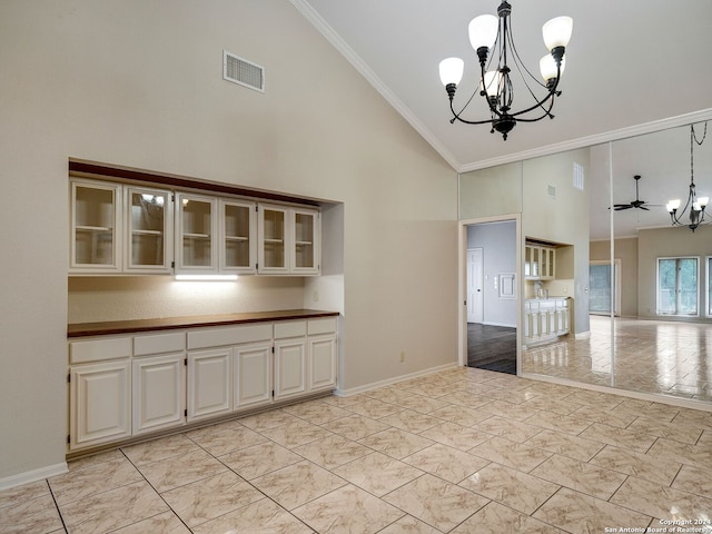 unfurnished dining area with ceiling fan with notable chandelier, high vaulted ceiling, and crown molding