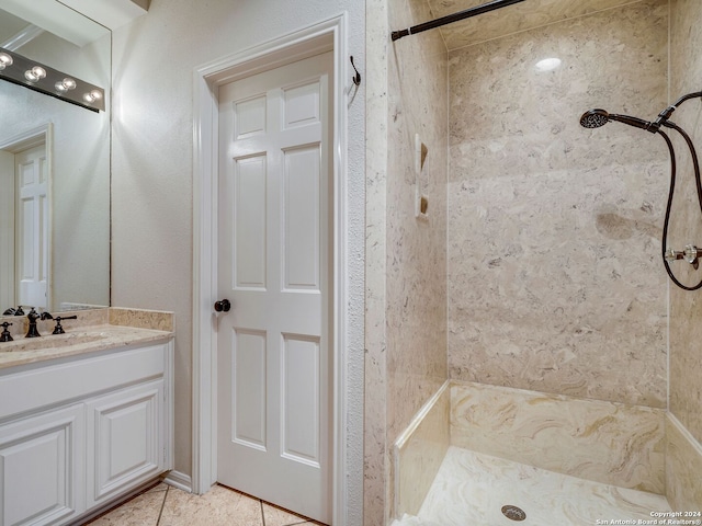 bathroom with tile patterned flooring, a tile shower, and vanity