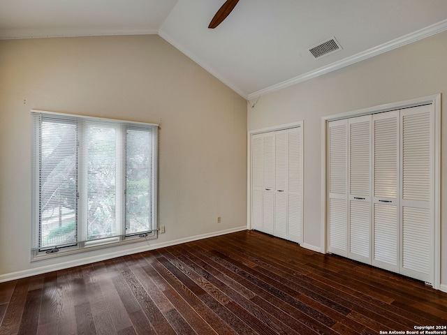 unfurnished bedroom featuring dark hardwood / wood-style flooring, ceiling fan, crown molding, lofted ceiling, and multiple closets