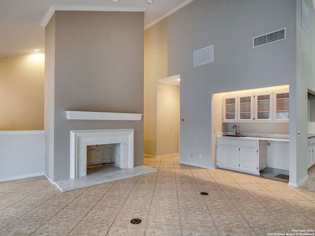 unfurnished living room with a fireplace, sink, a towering ceiling, and crown molding