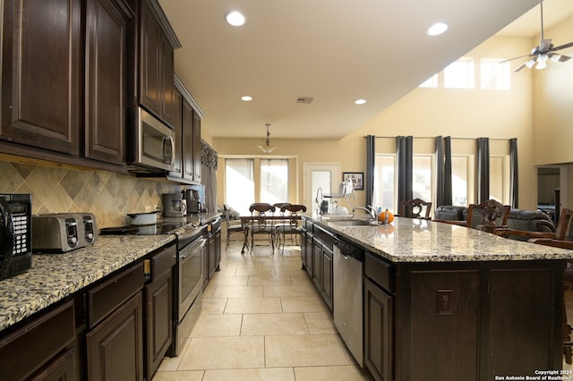 kitchen with light stone countertops, stainless steel appliances, sink, light tile patterned floors, and an island with sink