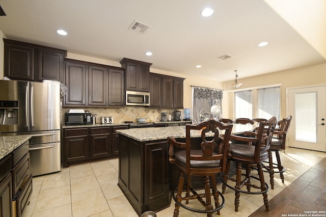 kitchen with light stone counters, a breakfast bar area, dark brown cabinets, a kitchen island, and appliances with stainless steel finishes