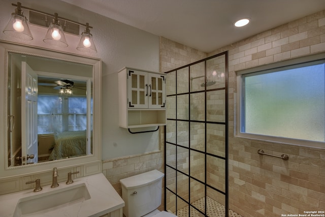 bathroom featuring a tile shower, vanity, ceiling fan, tile walls, and toilet