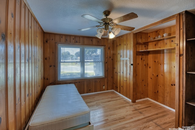 bedroom with a textured ceiling, light wood-type flooring, ceiling fan, and wood walls