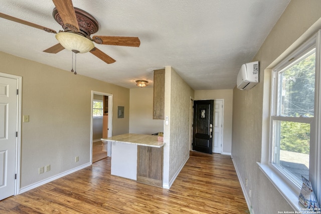 kitchen featuring ceiling fan, a wall mounted AC, kitchen peninsula, a textured ceiling, and light wood-type flooring