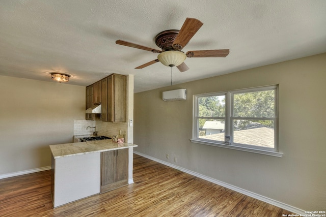 kitchen with backsplash, ceiling fan, a wall mounted AC, light hardwood / wood-style floors, and kitchen peninsula