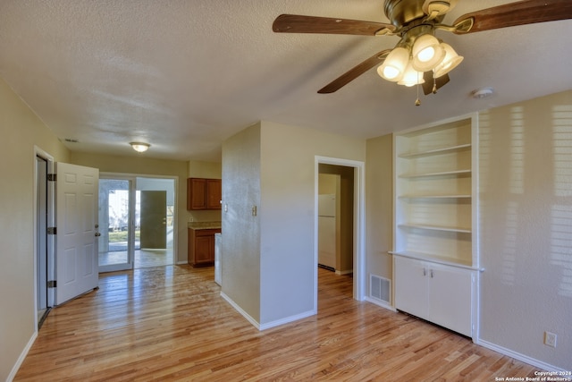 unfurnished living room with ceiling fan, built in features, a textured ceiling, and light wood-type flooring