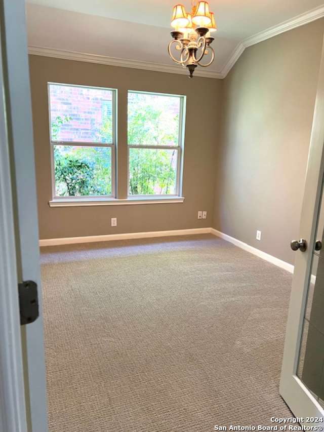 spare room with carpet flooring, a chandelier, lofted ceiling, and ornamental molding