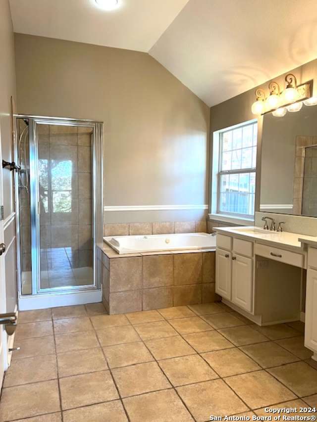 bathroom with tile patterned floors, plus walk in shower, vanity, and vaulted ceiling