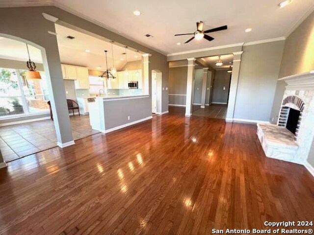 unfurnished living room with dark hardwood / wood-style flooring, decorative columns, ornamental molding, ceiling fan, and a fireplace