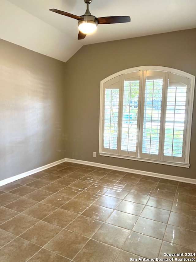 empty room with vaulted ceiling, dark tile patterned floors, and ceiling fan