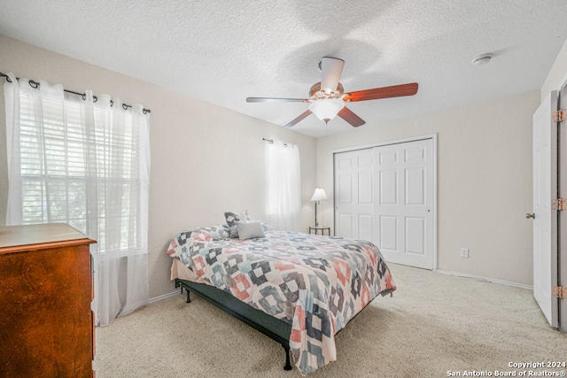 bedroom with a textured ceiling, ceiling fan, light carpet, and a closet