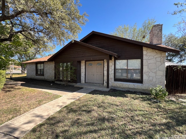 view of front facade with a front lawn, fence, stone siding, and a chimney