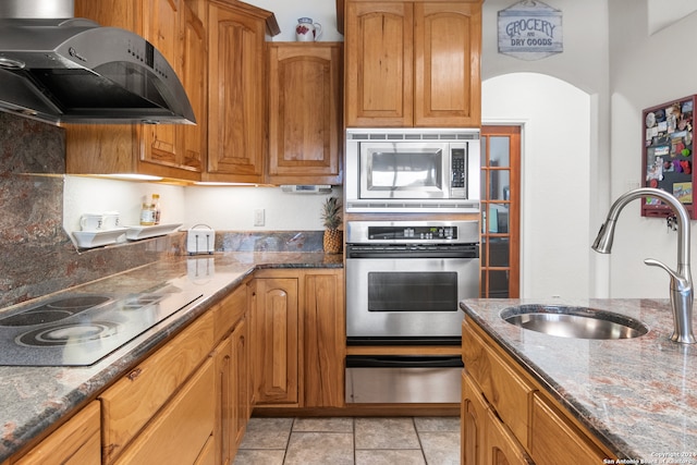 kitchen with ventilation hood, sink, dark stone countertops, and stainless steel appliances