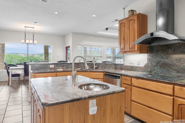 kitchen with dishwasher, wall chimney exhaust hood, stovetop, pendant lighting, and a center island with sink