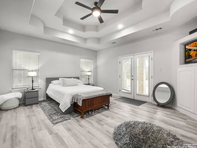 bedroom with ceiling fan, access to exterior, light hardwood / wood-style flooring, and a tray ceiling