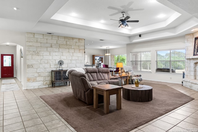 living room featuring a raised ceiling, ceiling fan, and light tile patterned floors