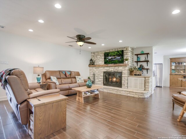 living room with a stone fireplace, ceiling fan, and wood-type flooring