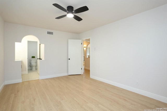 unfurnished bedroom with baseboards, visible vents, light wood finished floors, ensuite bath, and arched walkways