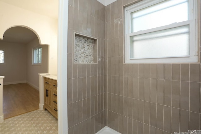 bathroom featuring baseboards, tiled shower, and vanity