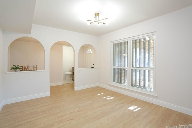 spare room featuring wood finished floors, baseboards, and a chandelier