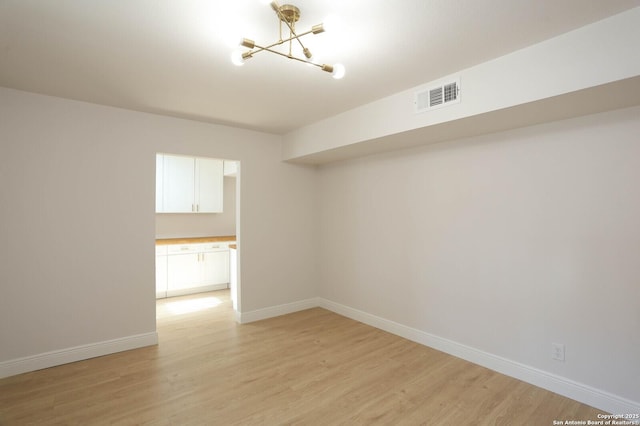 empty room featuring a notable chandelier, visible vents, light wood-style flooring, and baseboards