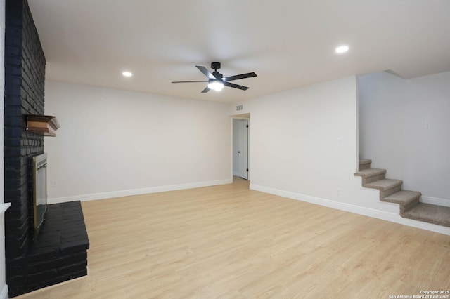 unfurnished living room with a ceiling fan, baseboards, a fireplace, stairs, and light wood-type flooring