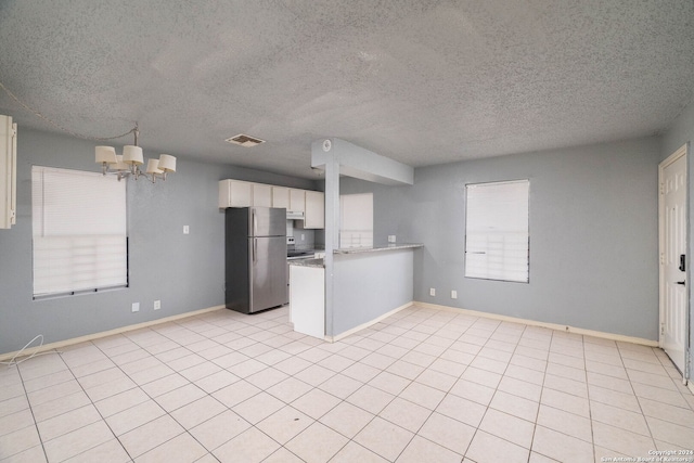 kitchen featuring white cabinets, a textured ceiling, kitchen peninsula, stainless steel refrigerator, and a chandelier