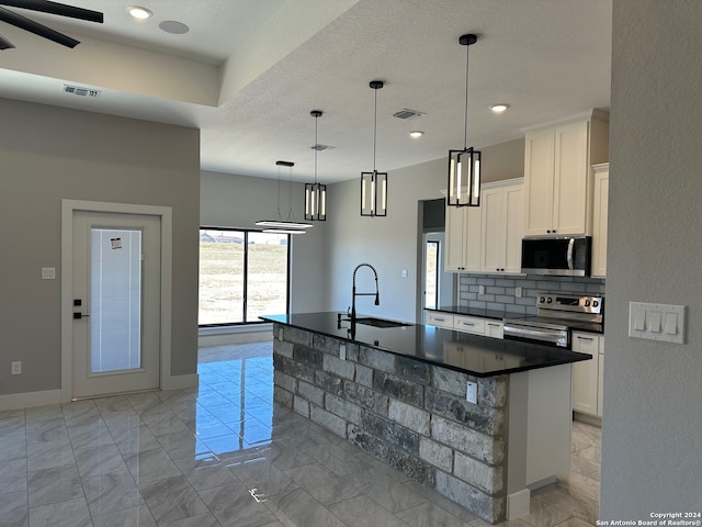 kitchen with sink, stainless steel appliances, tasteful backsplash, pendant lighting, and a center island with sink