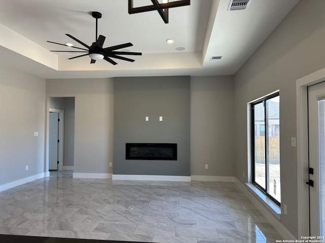 unfurnished living room featuring a raised ceiling and ceiling fan