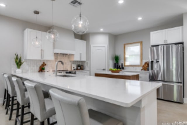 kitchen featuring kitchen peninsula, stainless steel refrigerator with ice dispenser, tasteful backsplash, decorative light fixtures, and white cabinetry