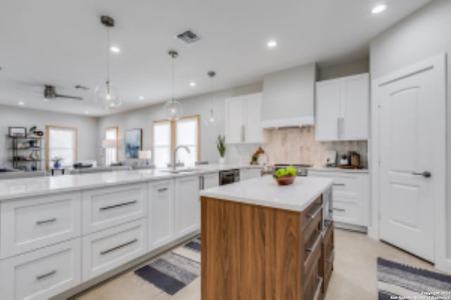 kitchen featuring a center island, premium range hood, white cabinets, hanging light fixtures, and decorative backsplash