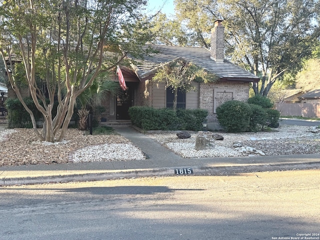 view of property hidden behind natural elements with a chimney, brick siding, and a tiled roof