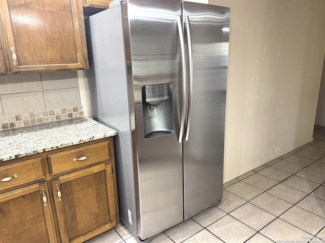 kitchen with light tile patterned floors, brown cabinetry, backsplash, and stainless steel fridge with ice dispenser