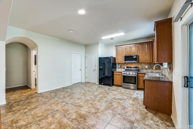 kitchen featuring appliances with stainless steel finishes, backsplash, tile patterned floors, dark stone counters, and sink