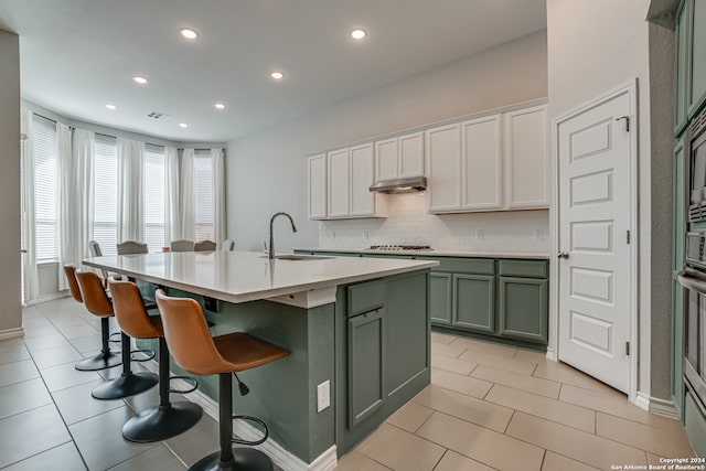 kitchen featuring white cabinetry, sink, tasteful backsplash, a breakfast bar area, and a kitchen island with sink