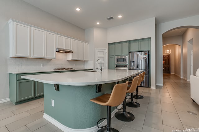 kitchen featuring appliances with stainless steel finishes, tasteful backsplash, a center island with sink, white cabinets, and a breakfast bar area