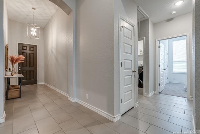 hall with a notable chandelier, light tile patterned flooring, and a textured ceiling