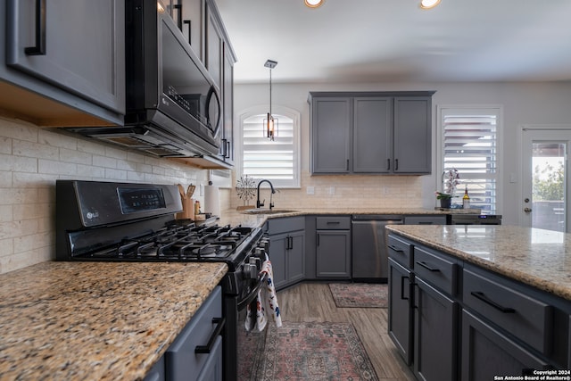 kitchen with hanging light fixtures, light stone counters, dark hardwood / wood-style flooring, backsplash, and black appliances