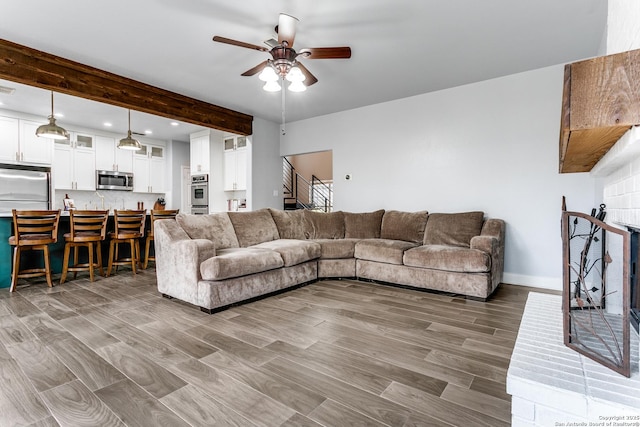 living room with beam ceiling, stairway, a ceiling fan, wood finished floors, and baseboards