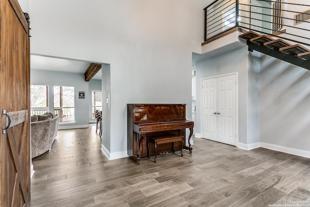 foyer featuring a barn door, wood finished floors, a towering ceiling, baseboards, and beamed ceiling