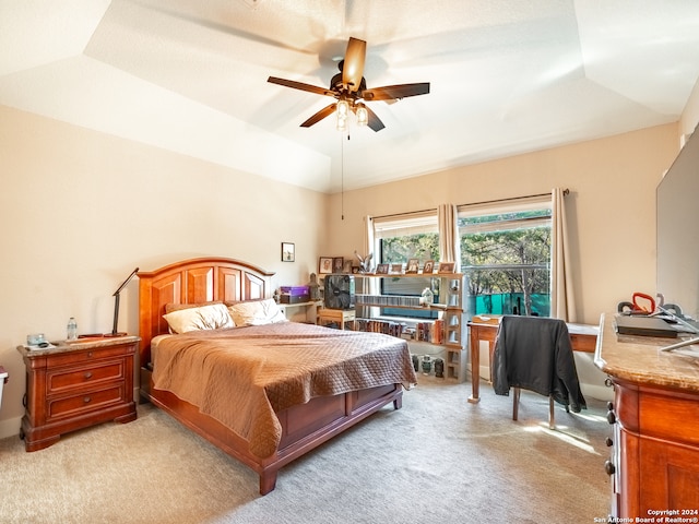 bedroom with light carpet, a tray ceiling, and ceiling fan