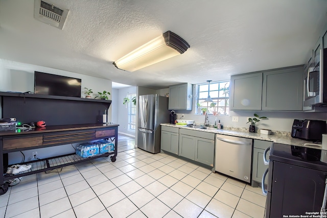 kitchen with a textured ceiling, stainless steel appliances, sink, light tile patterned floors, and gray cabinets