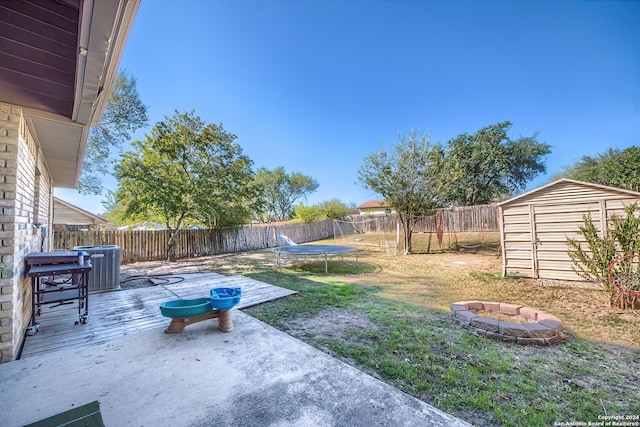 view of yard with a trampoline, a patio area, an outdoor fire pit, and a storage shed