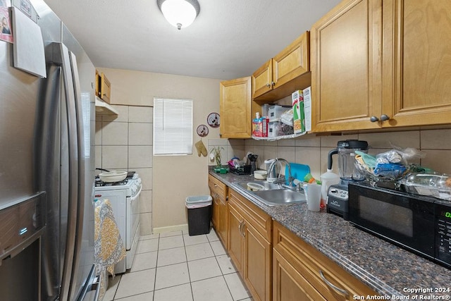 kitchen featuring stainless steel fridge, backsplash, sink, dark stone countertops, and white gas stove