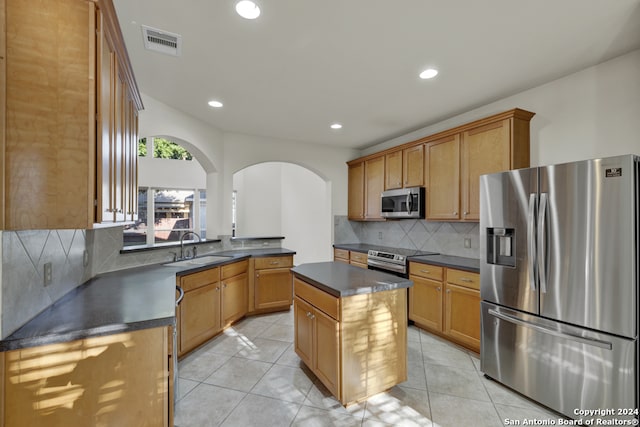 kitchen with light tile patterned flooring, backsplash, sink, a kitchen island, and stainless steel appliances