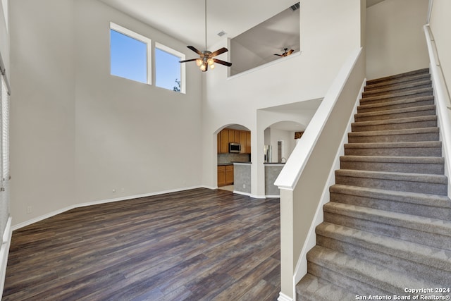 stairs with ceiling fan, a towering ceiling, and hardwood / wood-style flooring