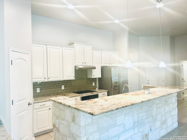 kitchen featuring light stone countertops, decorative light fixtures, white cabinets, stainless steel fridge with ice dispenser, and an island with sink